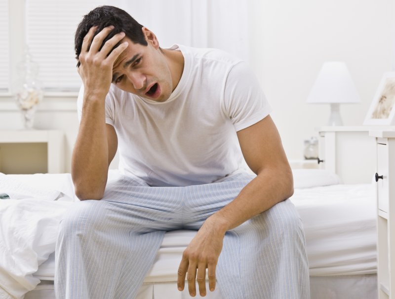 A man sitting on a bed and yawning.