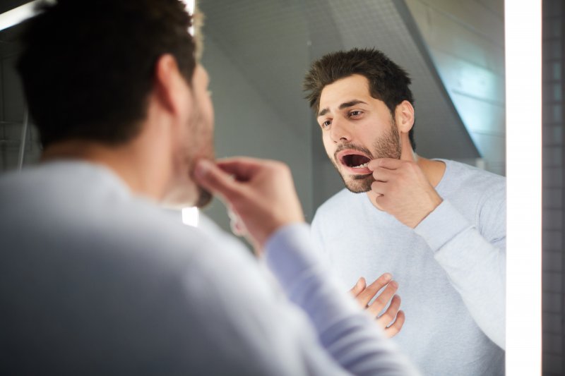 Man looking at teeth in mirror.